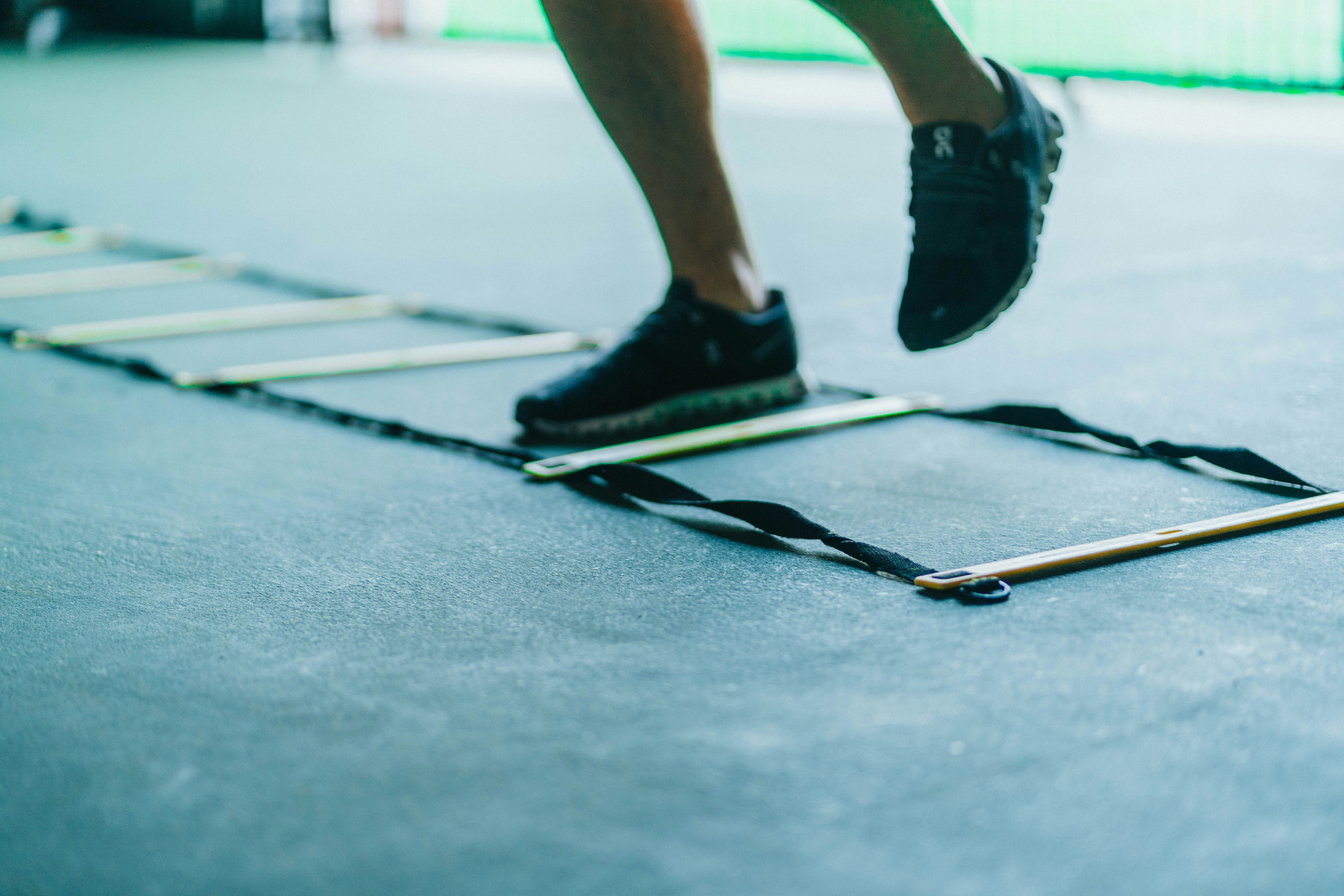 A young athlete performing quick-feet footwork through an agility ladder on an outdoor turf pitch — a coordination drill the research treats as a distinct skill from reactive, game-speed agility.
