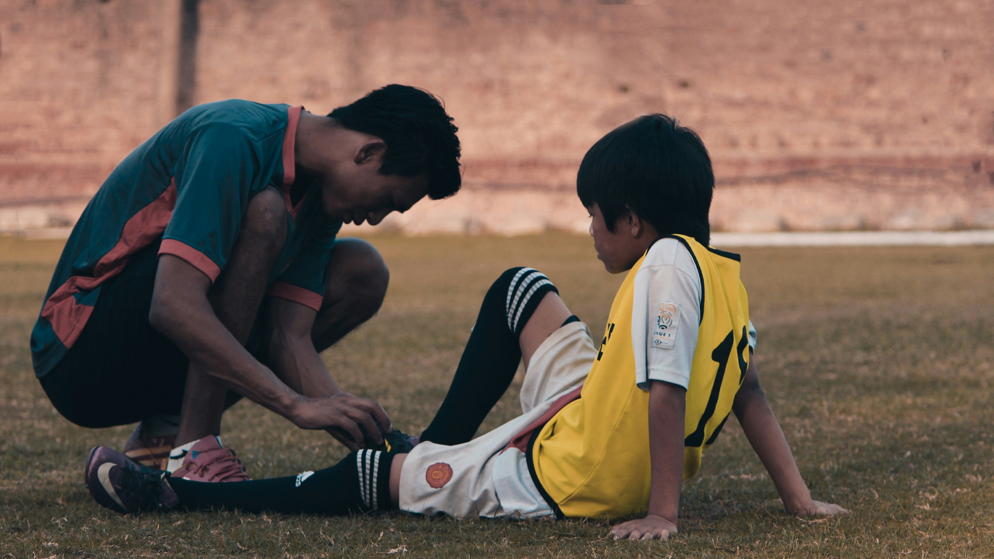 A young athlete pausing to hold their knee during training — the tibial tuberosity is one of several growth-plate attachment sites where rapid growth concentrates mechanical load first.