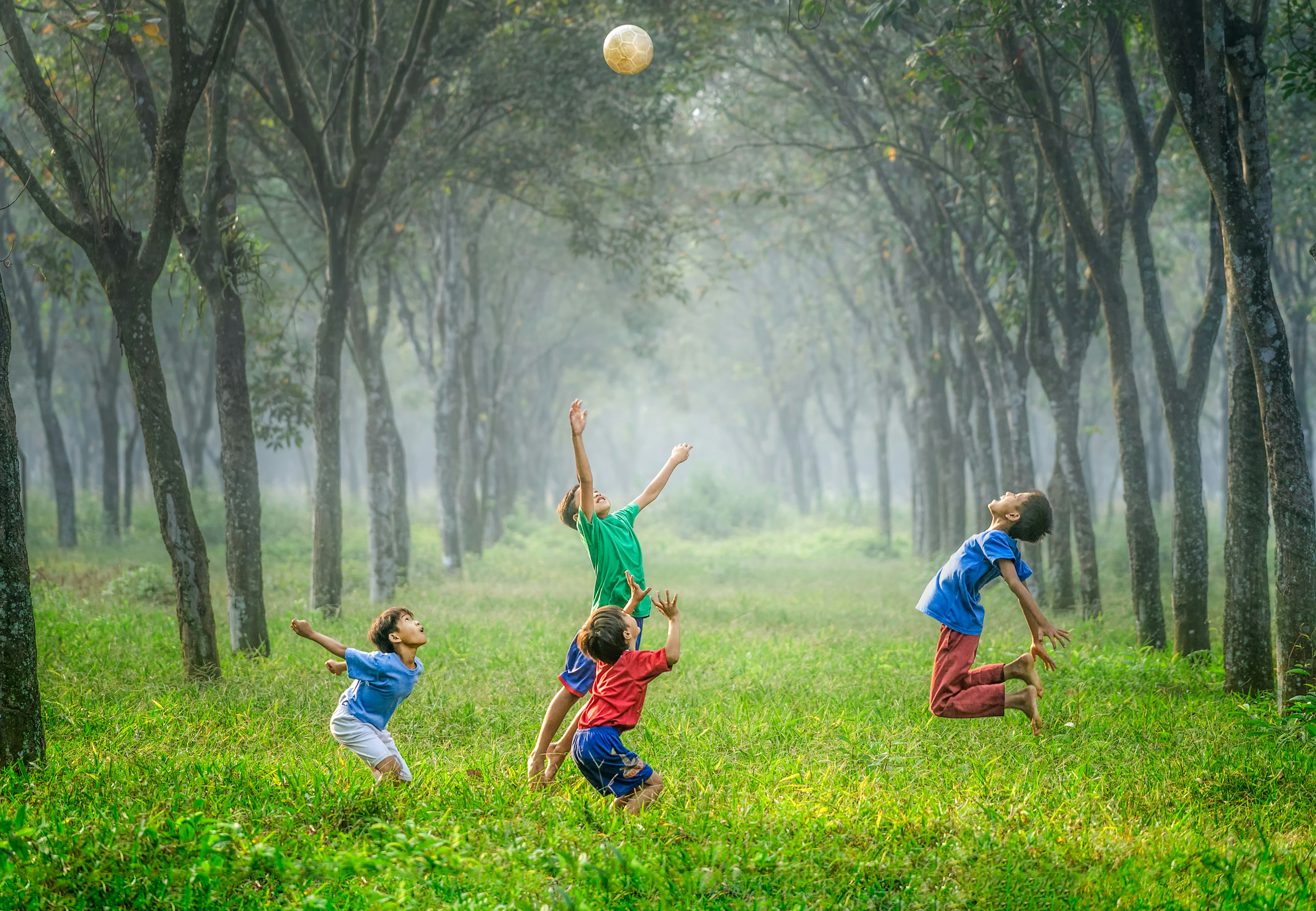 A young child confidently balancing along a low beam during a PE class, watched by an encouraging instructor — physical competence and confidence together are exactly what physical literacy names as a single construct.